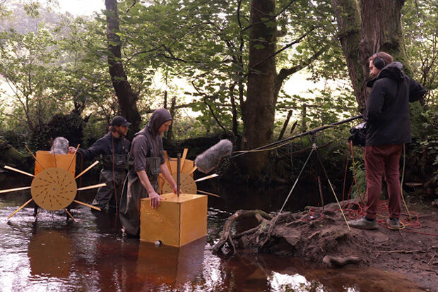 Men with wooden contraptions being recorded in a stream