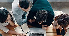 academics huddled round a desk using a laptop and notebook