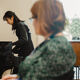 Arts PhD student playing the piano observed by a member of staff