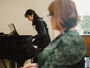 Arts PhD student playing the piano observed by a member of staff