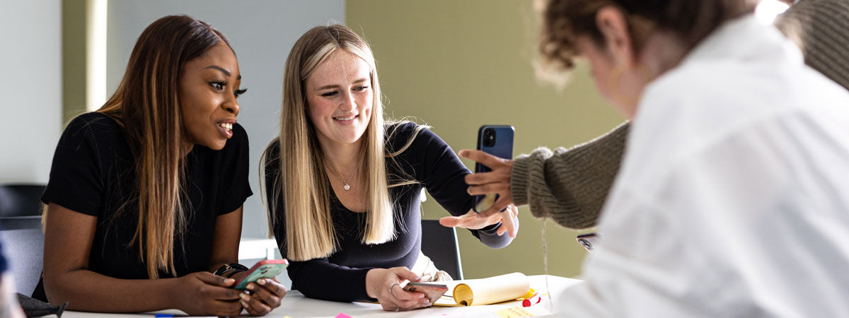 Students look at their mobile phone and smile instead of looking at the work on the desk