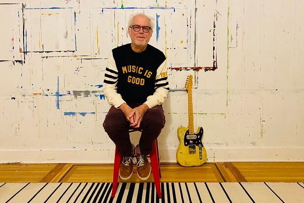 Bill Frisell sat on chair with guitar in background