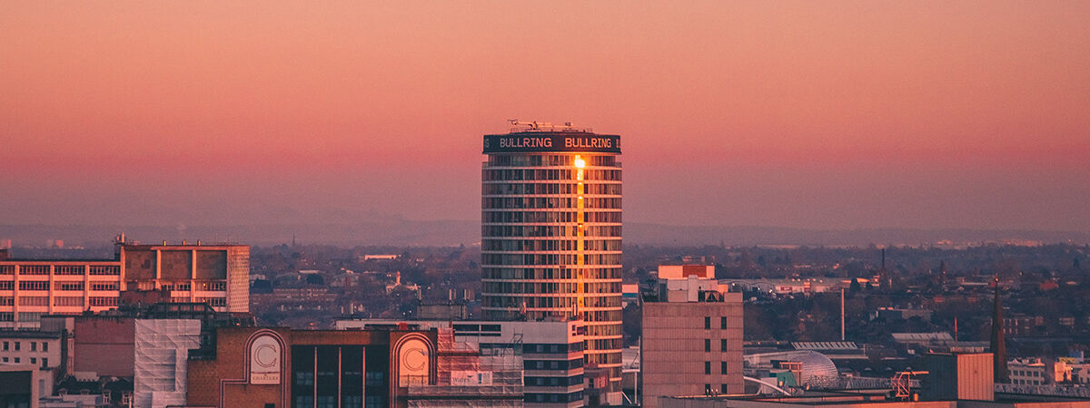 The Birmingham skyline at sunset. The sky fades from pink to blue and the setting sunlight glints off the Rotunda building.