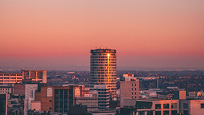 The Birmingham skyline at sunset. The sky fades from pink to blue and the setting sunlight glints off the Rotunda building.