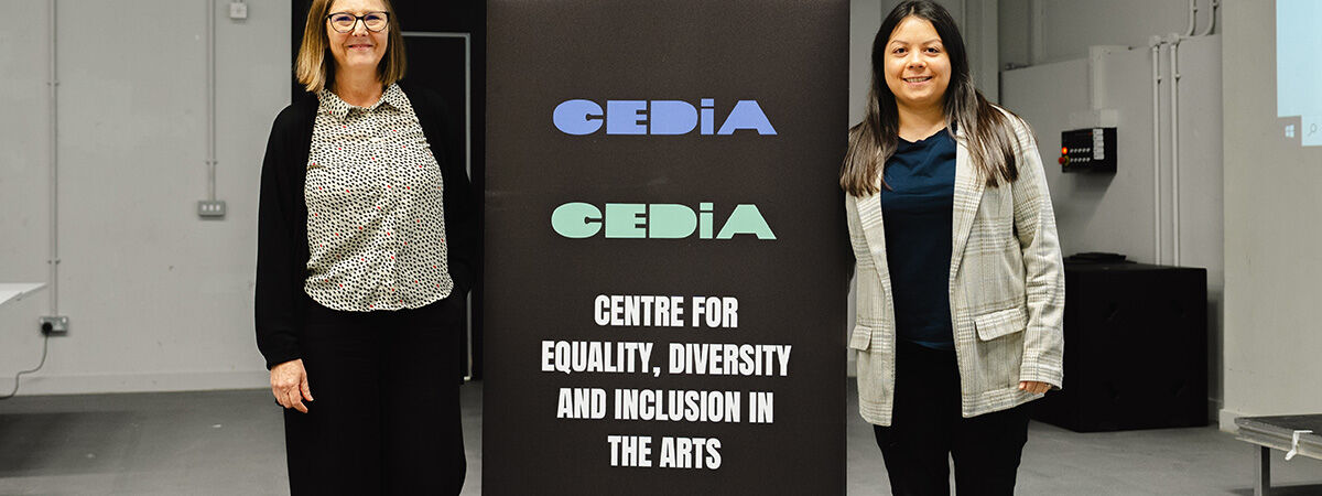 Two academics stand next to a stand for the centre for equality diversity and inclusion in the arts