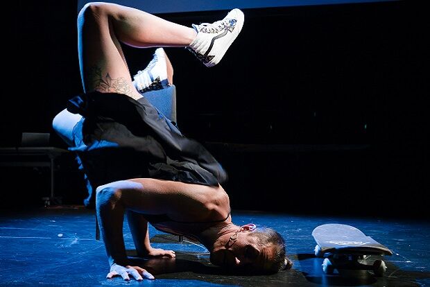 Stage performer doing headstand next to skateboard