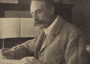 Black and white image of Edward Elgar, English composer, sat at a desk