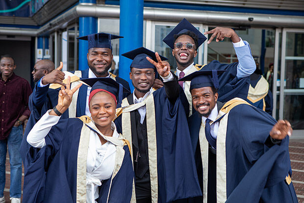 A group of black students in graduation gowns and smiling for photo