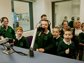 Children recording a podcast around the microphones in Birmingham City University's radio studios