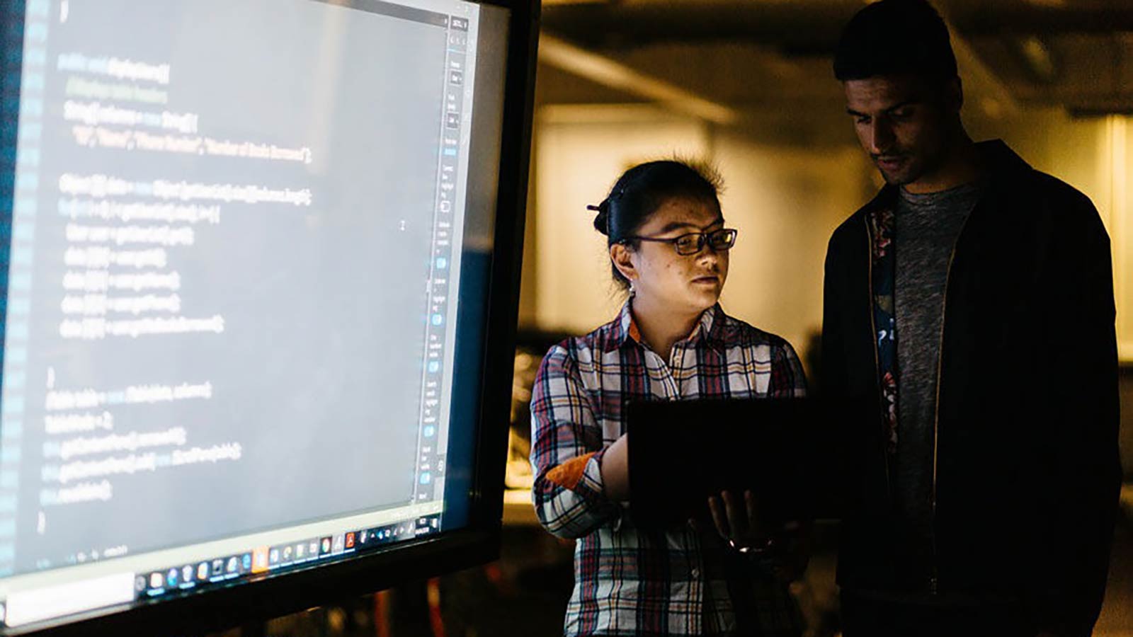 Two students working on a large screen to edit code