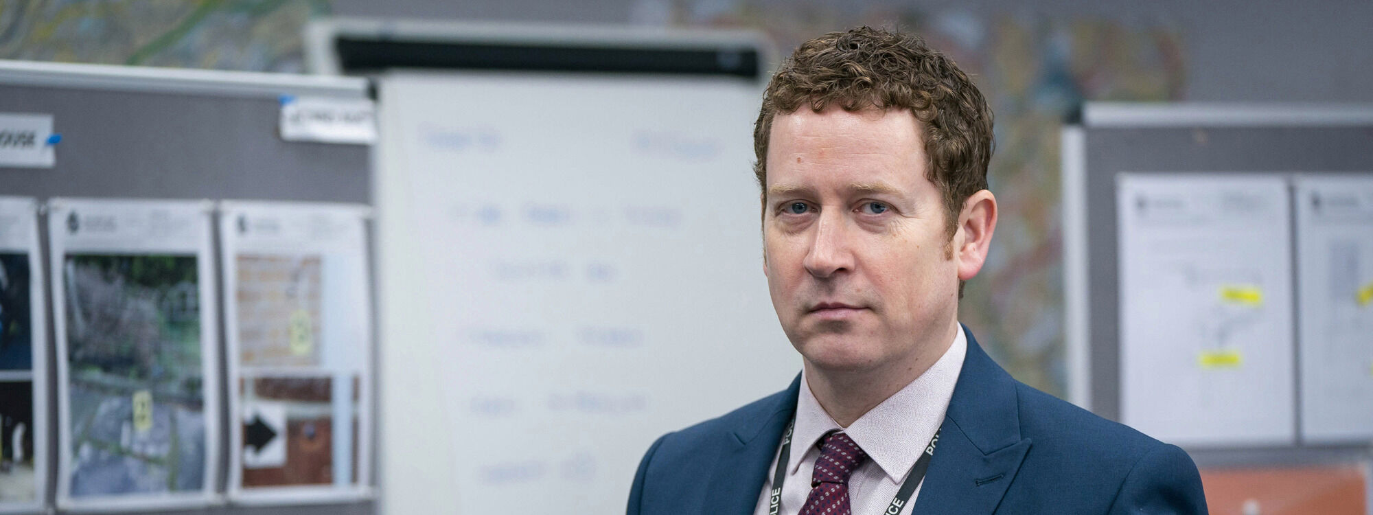Image of Line of Duty actor Nigel Boyle in character as Ian Buckells, pictured from the chest up in the police station wearing a suit
