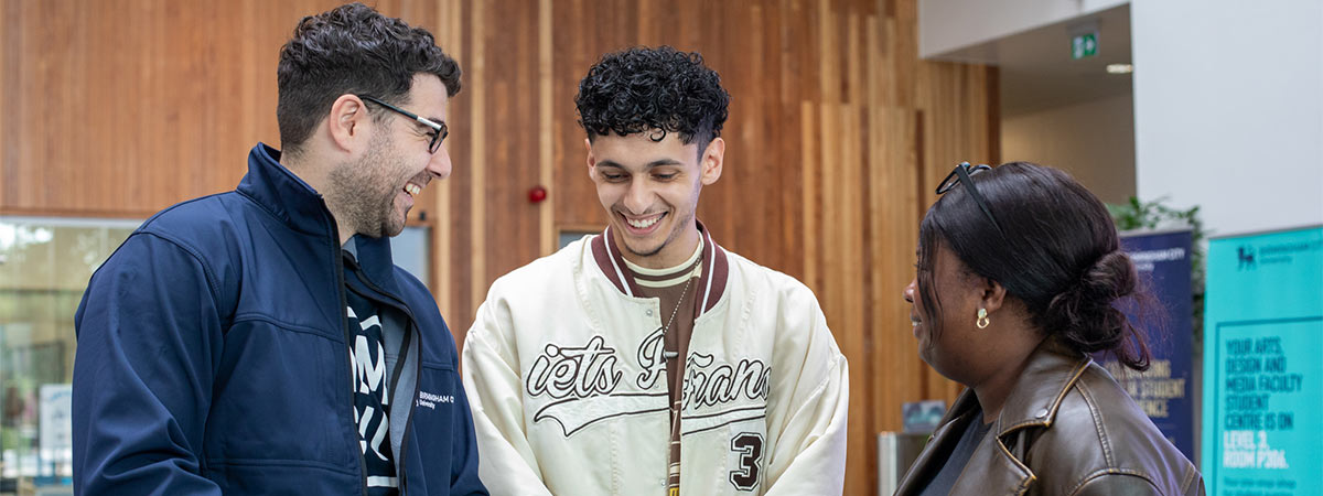 A member of BCU staff helping two visitors at an open day