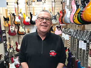 A man smiling at the camera in a guitar shop