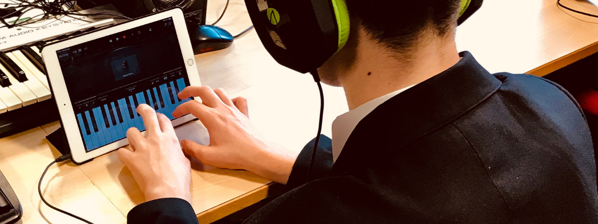Picture of an Ipad and a student in headphone playing on a piano app