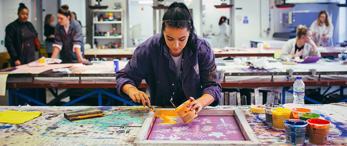 A student in a printmaking class painting the printing screen with paint.