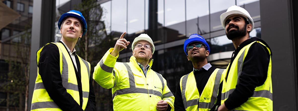 Four  people in hard hats and high vis pointing up