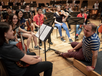 Musicians from the Junior Conservatoire taking a break during tutoing. The conductor is sitting on the floor and talking to young people holding musical instruments