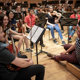 Musicians from the Junior Conservatoire taking a break during tutoing. The conductor is sitting on the floor and talking to young people holding musical instruments