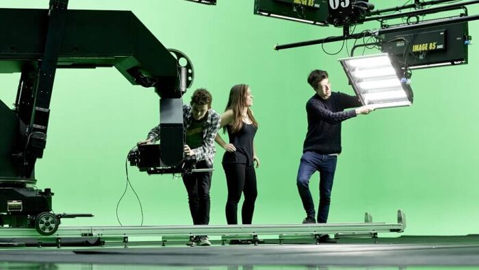 Three students setting up the lights and robotic camera arm in the green screen studio.