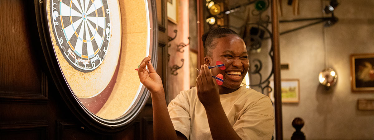 Smiling student collecting darts from a dart board at Flight Club