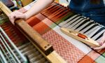 Student at weaving loom creating complex fabric design in red, white, green and blue