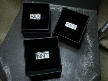 Three silver rings sit in black boxes. They sayy: Bab, Pride and Innit