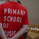 A child is wearing a red t-shirt with white text that reads 'Primary School of Music'